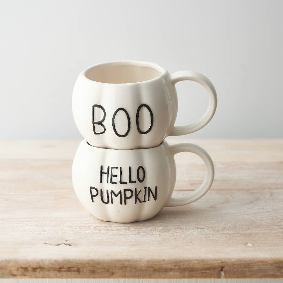 Two white mugs with 'BOO' and 'HELLO PUMPKIN' text on a wooden surface.
