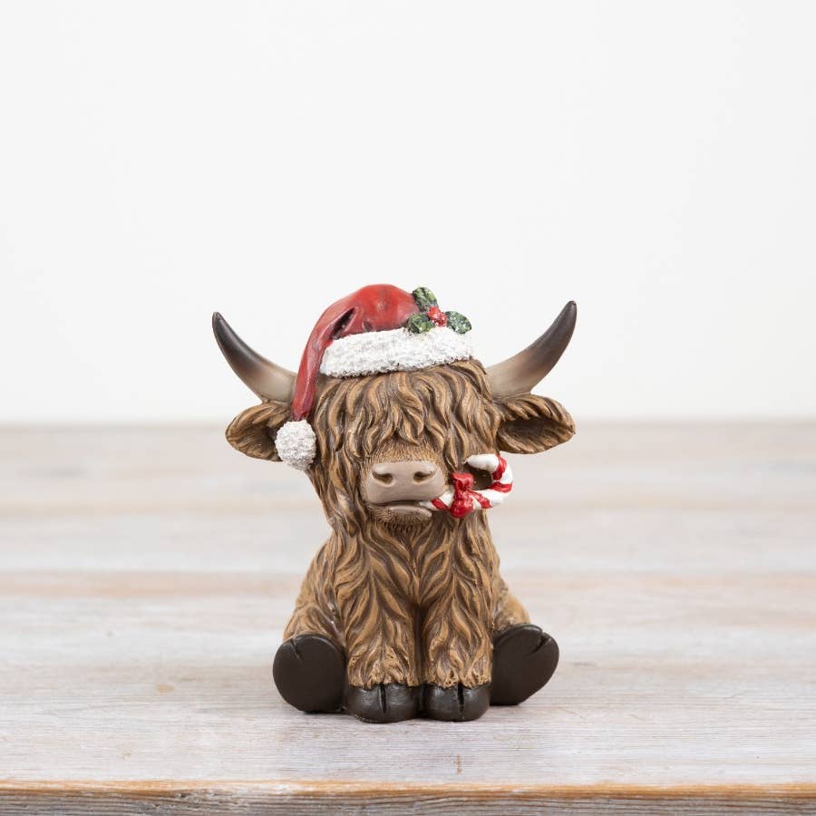 Festive figurine of a highland cow wearing a Santa hat on a wooden surface