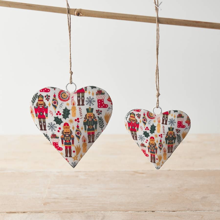 Two heart-shaped Christmas decorations with nutcracker pattern hanging on a wooden surface.