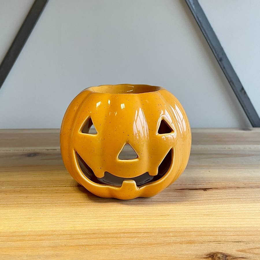 Orange ceramic pumpkin with a face on a wooden surface