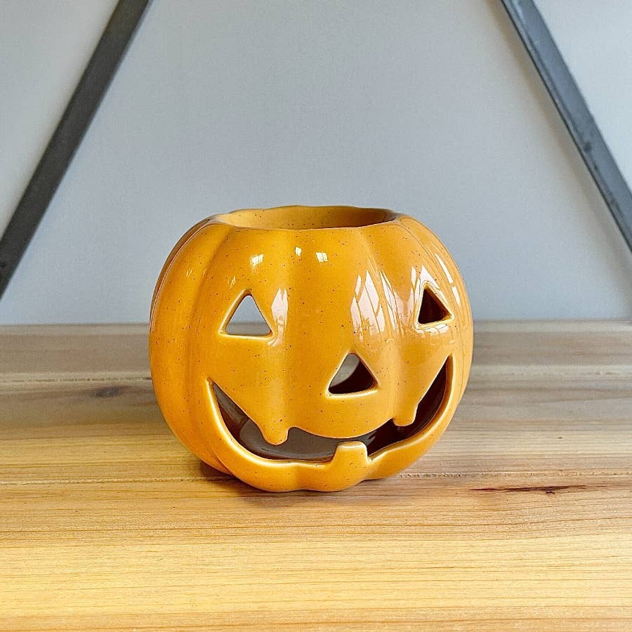 Orange ceramic jack-o'-lantern on a wooden surface with a neutral background