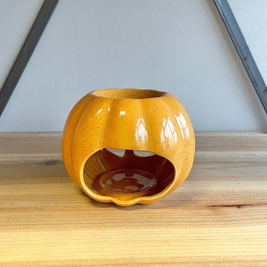Orange ceramic pumpkin oil burner on a wooden surface with a neutral background