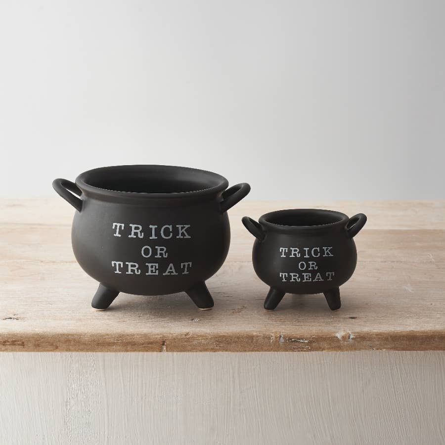 Two black 'Trick or Treat' cauldron ornaments on a wooden surface with a light background