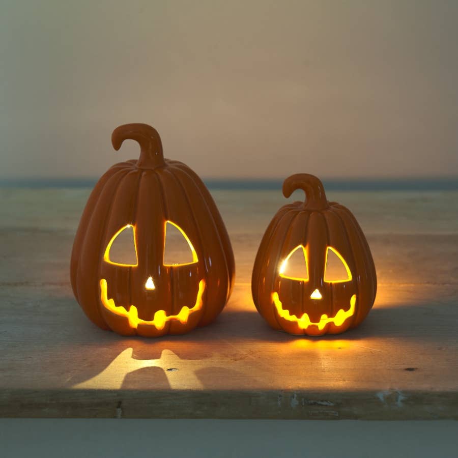 Two lit pumpkin decorations on a wooden surface with a neutral background