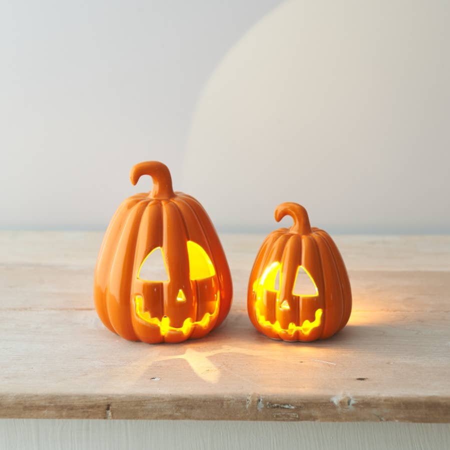 Two lit pumpkin decorations on a wooden surface with a neutral background
