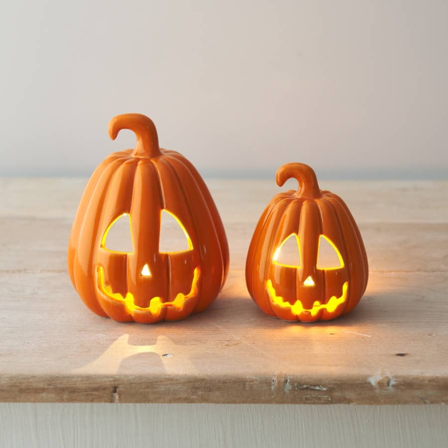 Two lit pumpkin decorations on a wooden surface with a neutral background