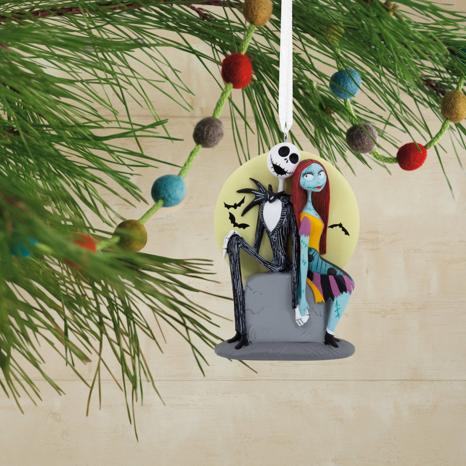 Disney The Nightmare Before Christmas Jack & Sally Christmas ornament hanging from a Christmas tree in the background.