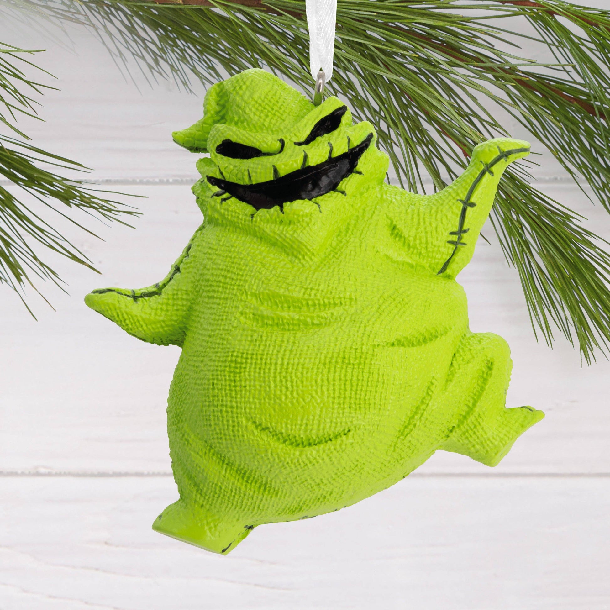 Green The Nightmare Before Christmas Oogie Boogie Christmas ornament hanging from Christmas tree in the background.