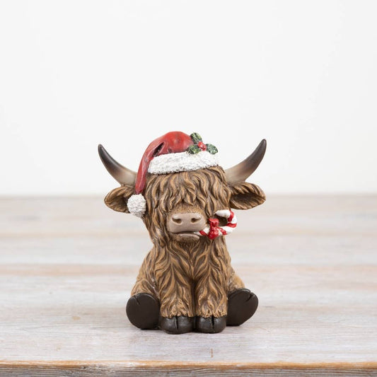 Festive figurine of a highland cow wearing a Santa hat on a wooden surface