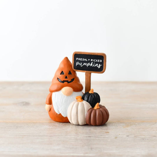 Halloween-themed gnome with pumpkins and a sign on a wooden surface