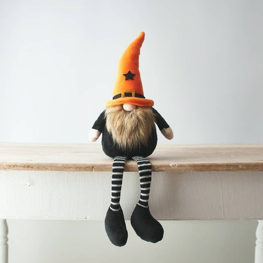 Gnome figurine with an orange hat and striped socks sitting on a wooden surface.