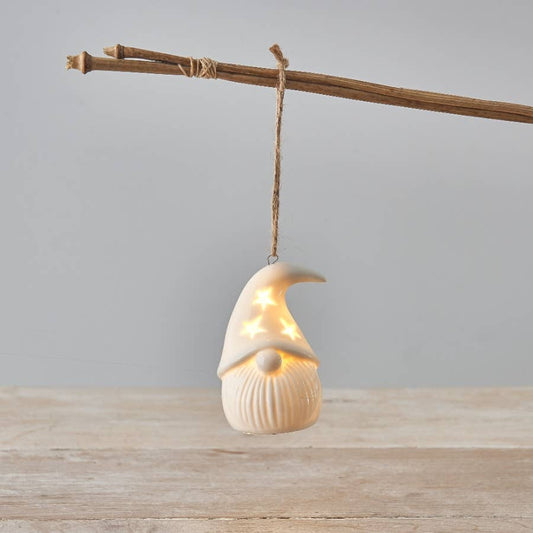 Decorative gonk light hanging from a branch on a wooden surface with a gray background