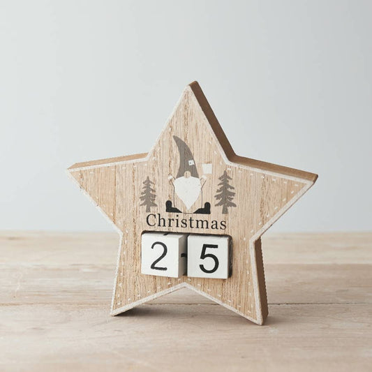 Wooden star-shaped Christmas countdown decoration with a gnome and trees design on a light background